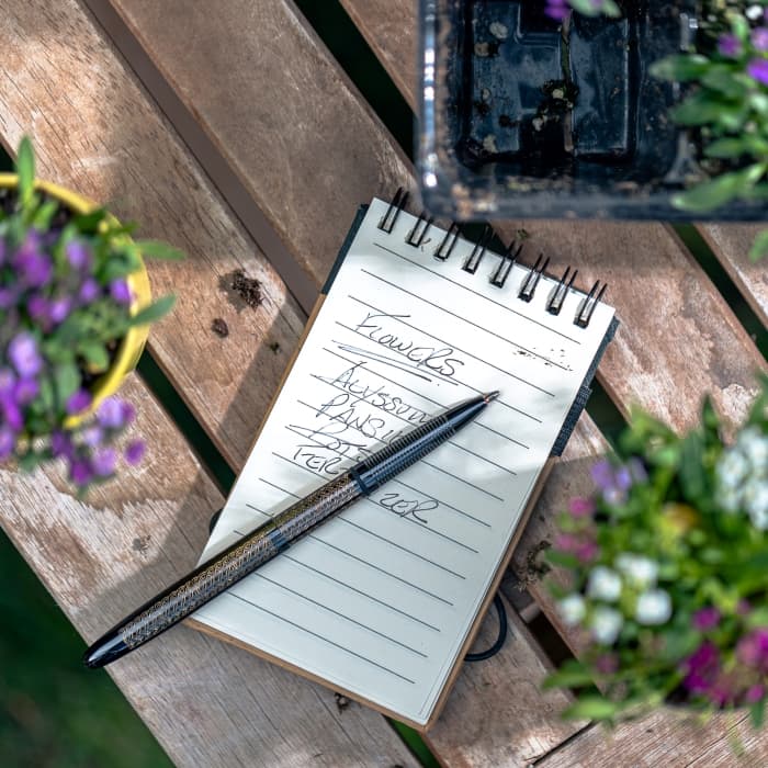 Open 400BTN-CK black titanium nitride bullet with Celtic knot engraving laying atop a small lined notebook. There are flowerpots with purple flowers surrounding the notebook.