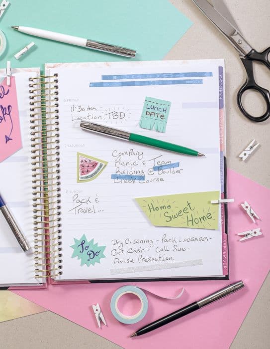 White, Green, and Black cap-o-matic space pens with chrome accents laying atop a lined, spiral planner.